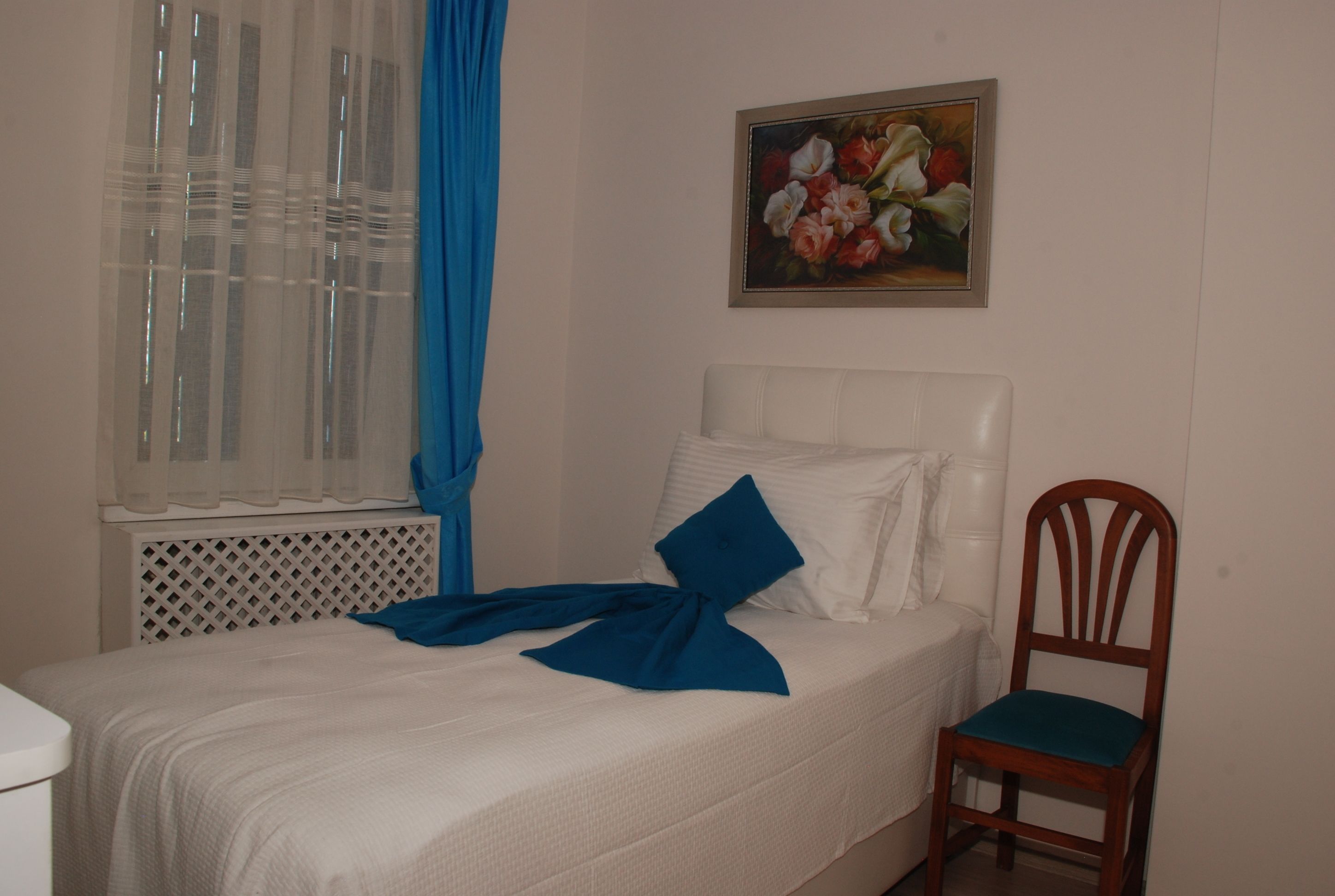 Un dormitorio con cama, una silla, un ventanal con cortinas y un cuadro en la pared.