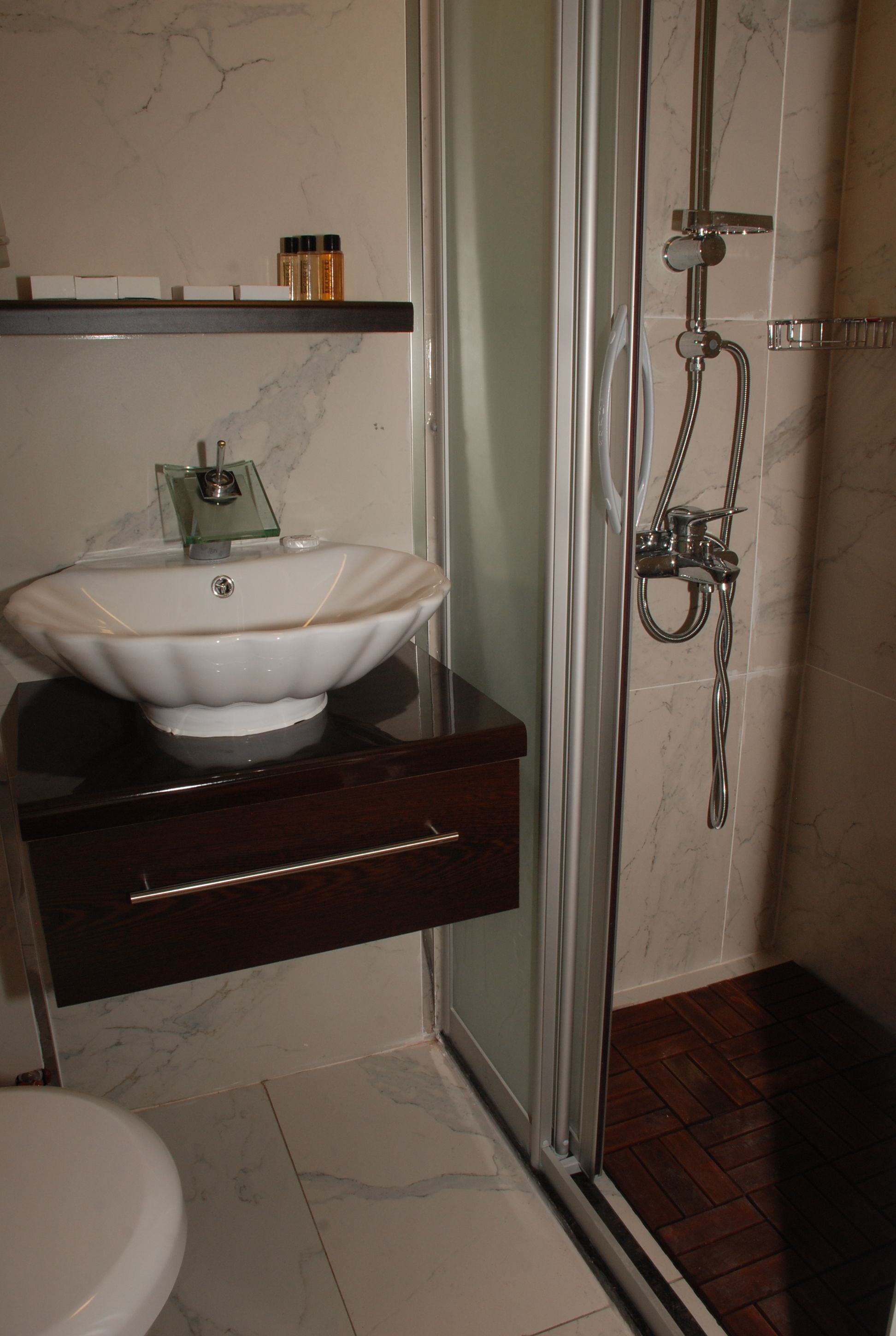 A bathroom with a marble sink, a glass shower enclosure, and a wooden vanity.