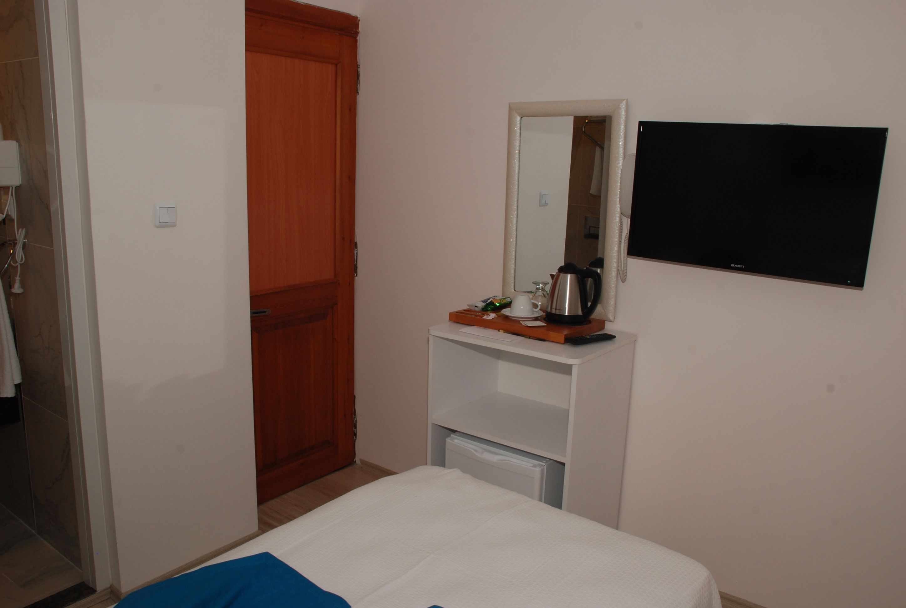 Une chambre d’hôtel comprenant un lit, une armoire en bois, une table de chevet blanche avec un miroir, une télévision et une machine à café.