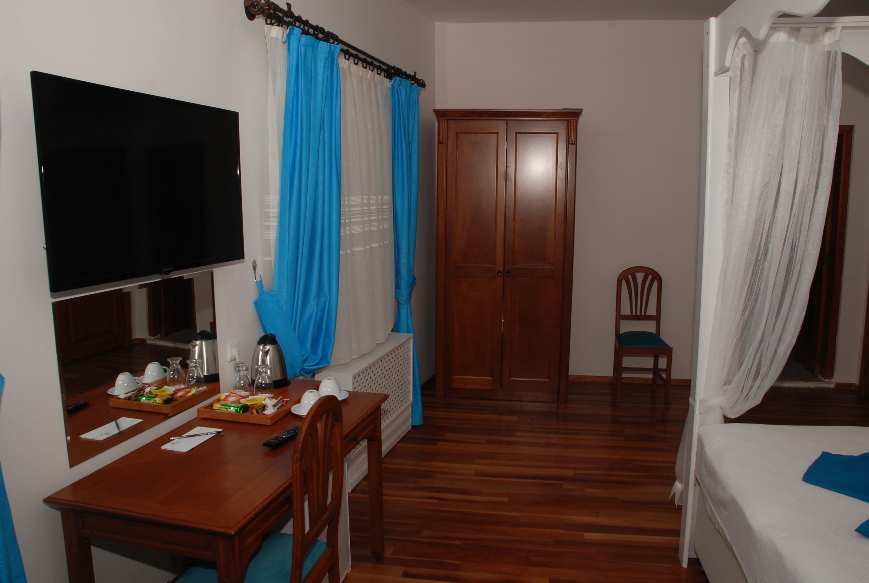 A hotel room with a wooden desk, a television, a wardrobe, a bed, and a chair.