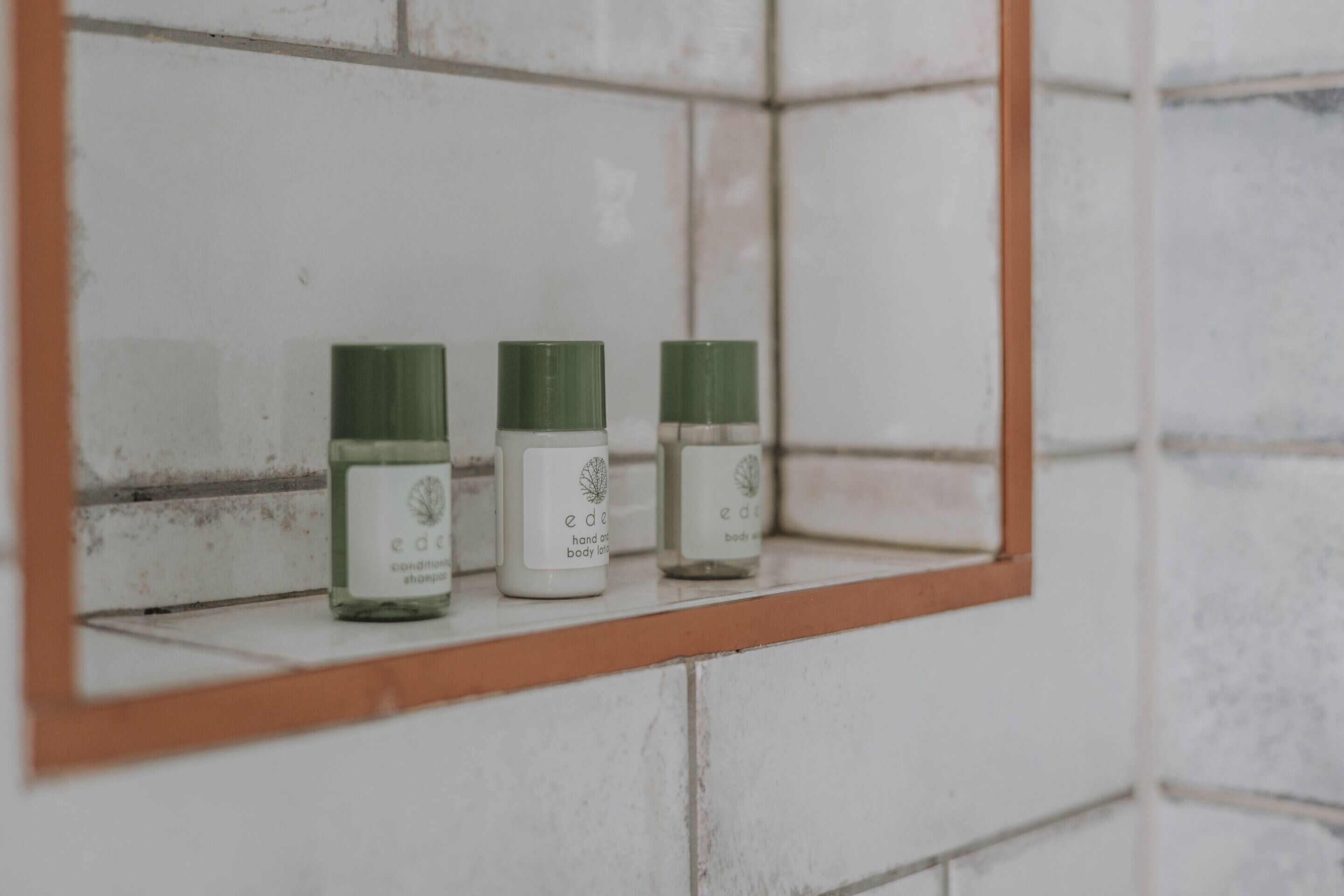 Three bottles of 'e' body lotion on a white tiled shelf.
