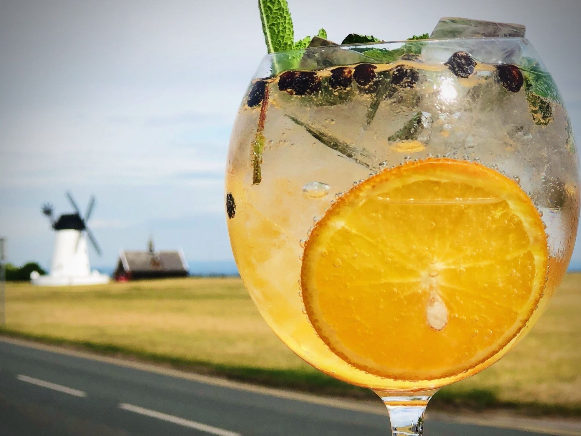 A glass of drink with a slice of orange and mint leaves, with a windmill in the background.