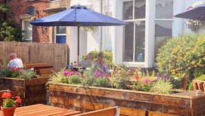 An outdoor seating area with wooden benches and raised planters with flowers. - The Queens Hotel Lytham (Lytham St. Anne's)