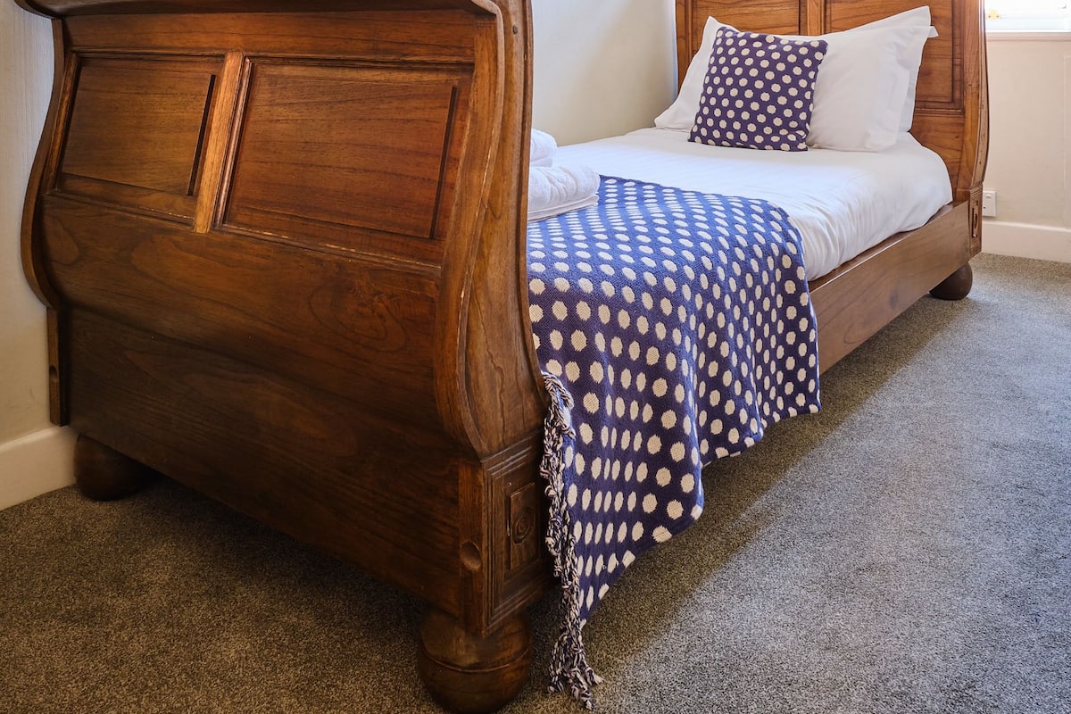 Una cama de madera con cabecera, un colchón blanco y una manta azul con lunares.