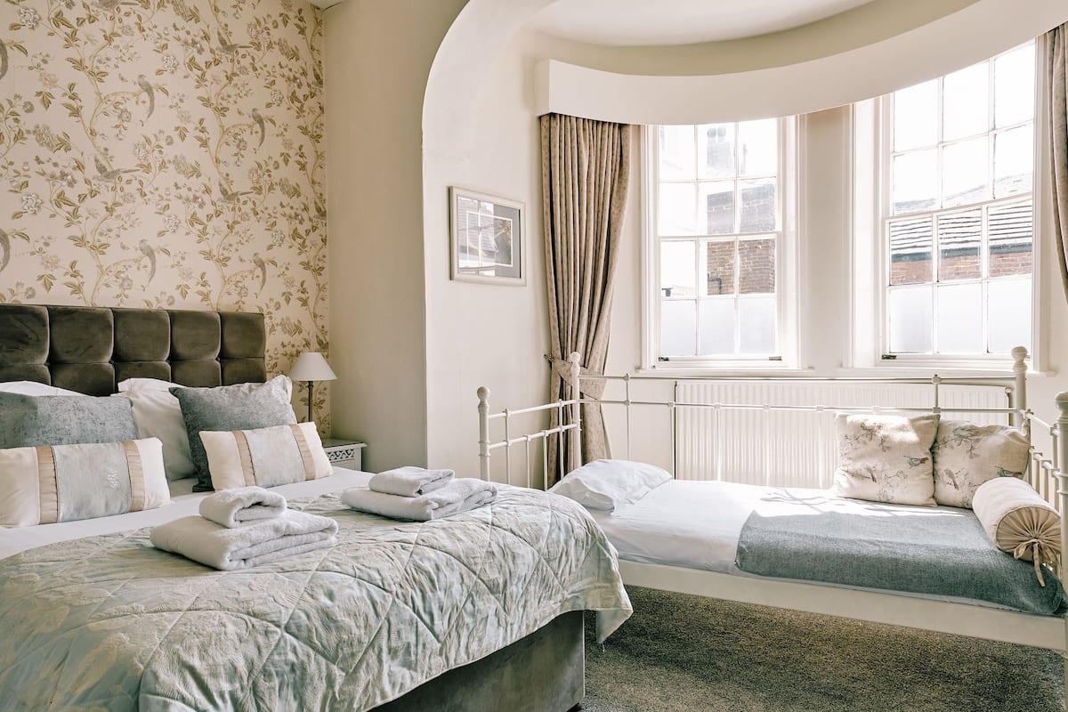 Un dormitorio con una cama grande, una cama más pequeña y una ventana con cortinas.