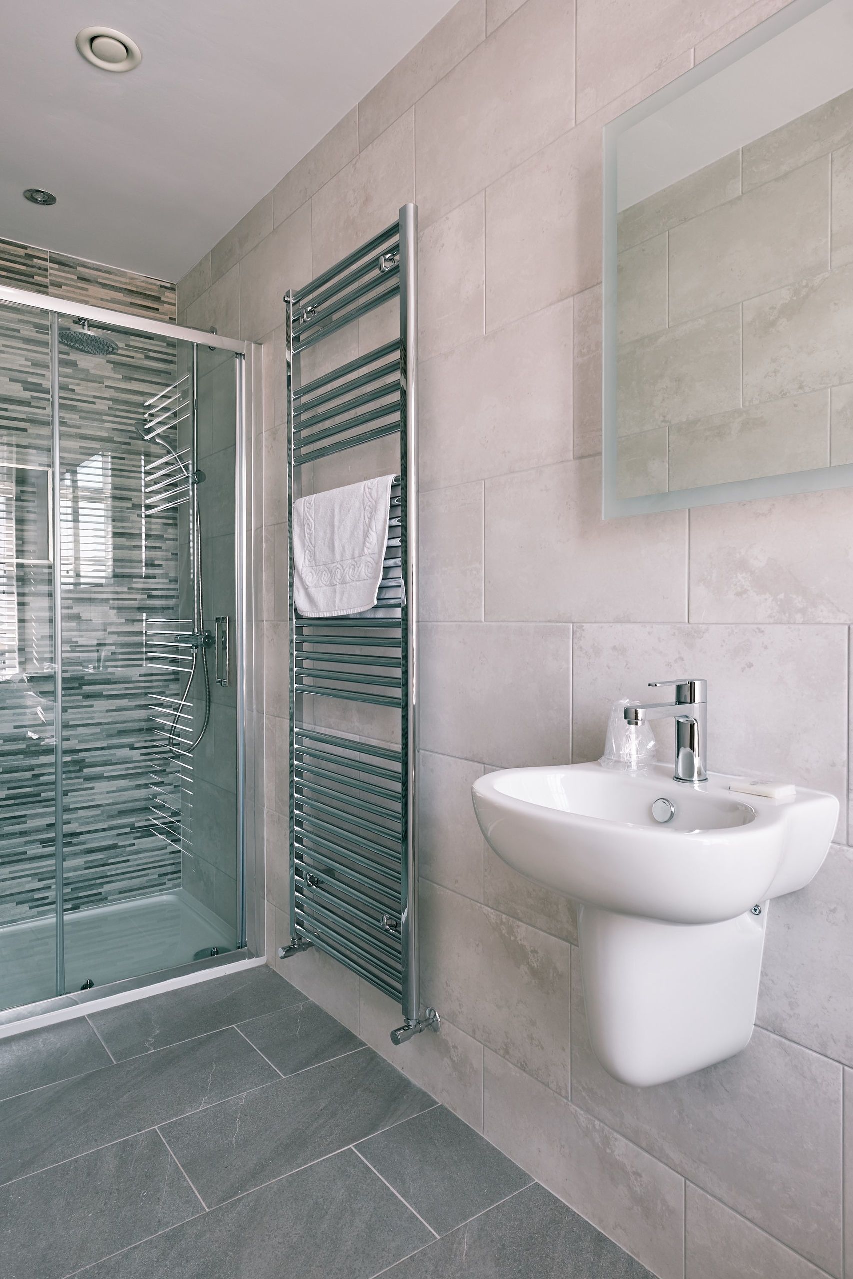 A modern bathroom with a glass shower enclosure, a towel rack with a white towel, and a white sink with a mirror above it.