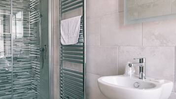 Un baño moderno con cabina de ducha de vidrio, un perchero con una toalla blanca y un lavamanos blanco con un espejo encima.