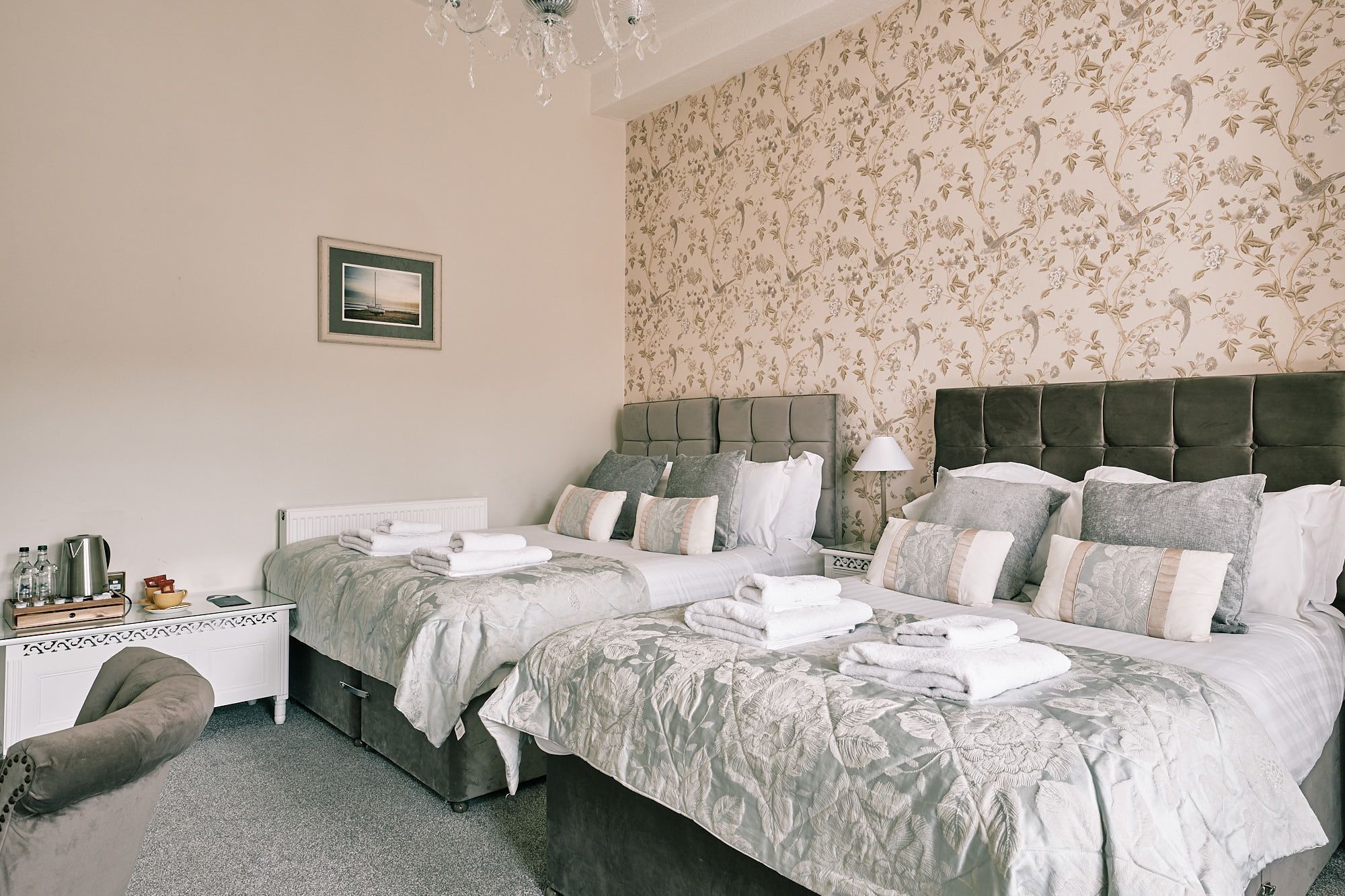 A double bed with a floral bedspread, a bedside table with a lamp, and a framed picture on the wall.