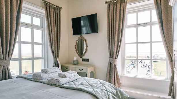 A hotel room with a bed, a TV, a mirror, and a window with curtains. - The Queens Hotel Lytham (Lytham St. Anne's)
