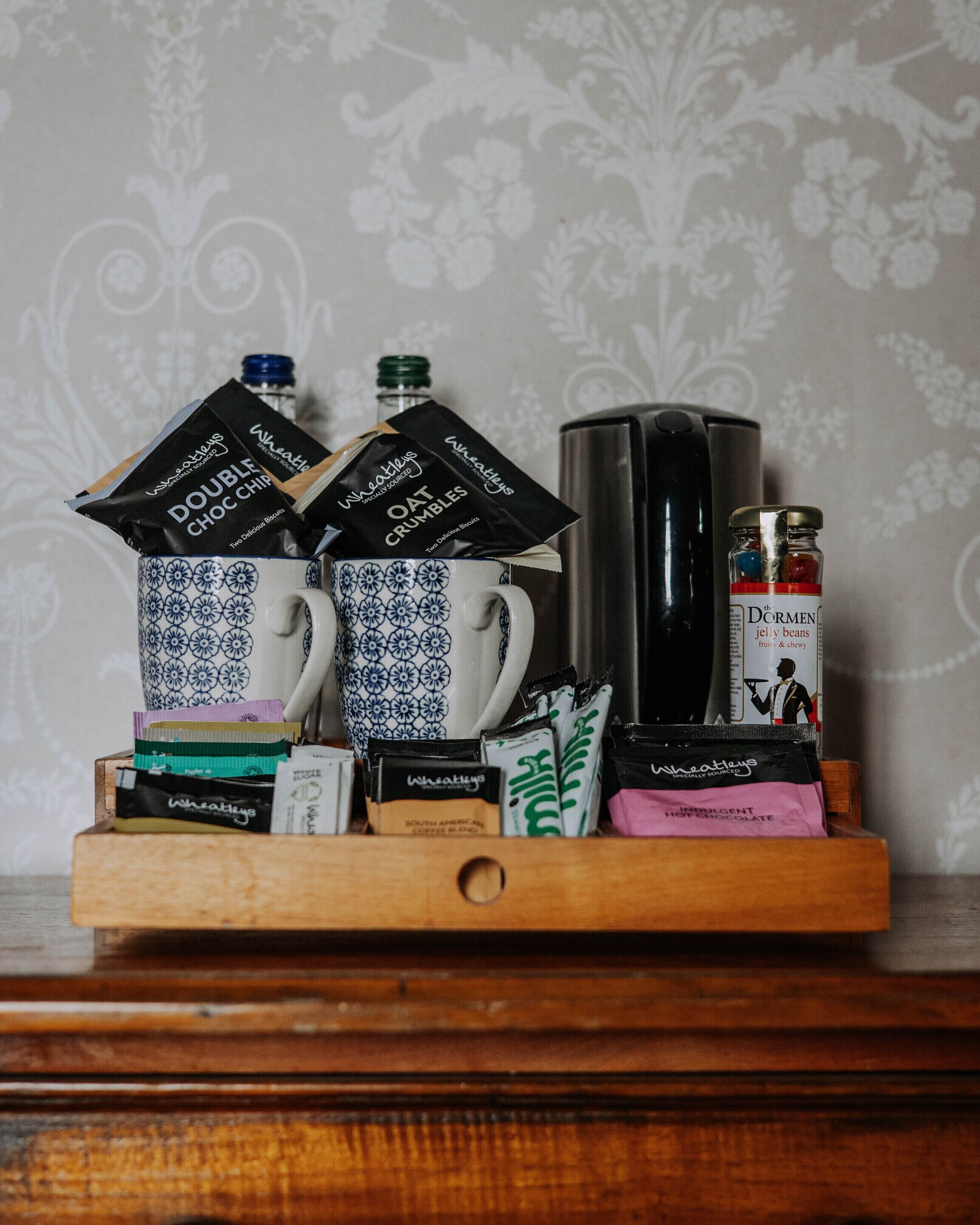 A tray with coffee mugs, tea bags, and a jar of jelly beans.