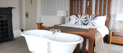 A bedroom with a wooden bed, white bedding, a white bathtub, and a radiator.