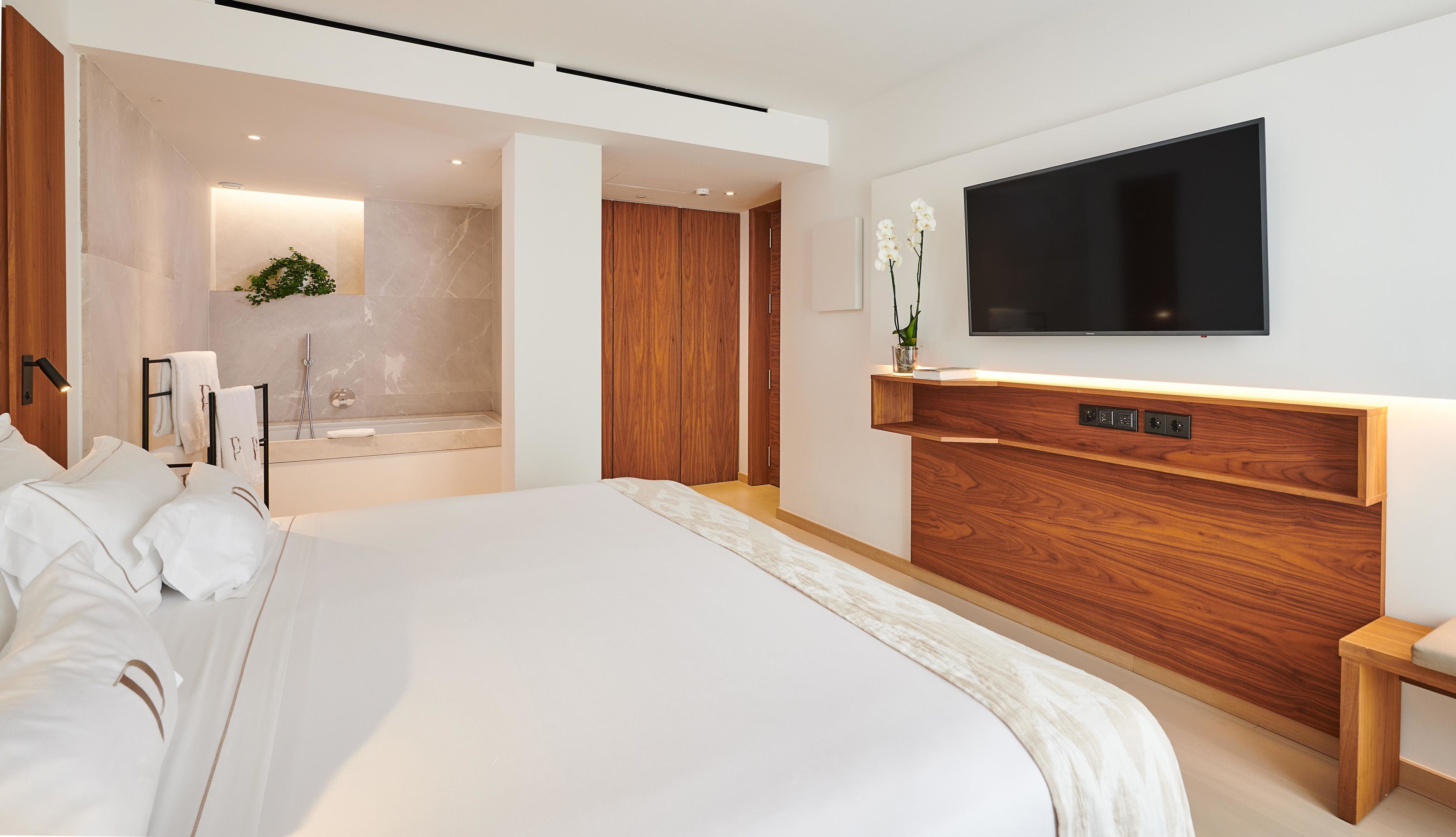 Een moderne hotelkamer met een groot bed, een ingebouwde televisie, een houten opbergmeubel en een aparte badkamer met bad.