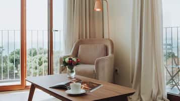 A room with a sofa, a table with a book and a cup, a chair, a lamp, and a balcony with curtains.
