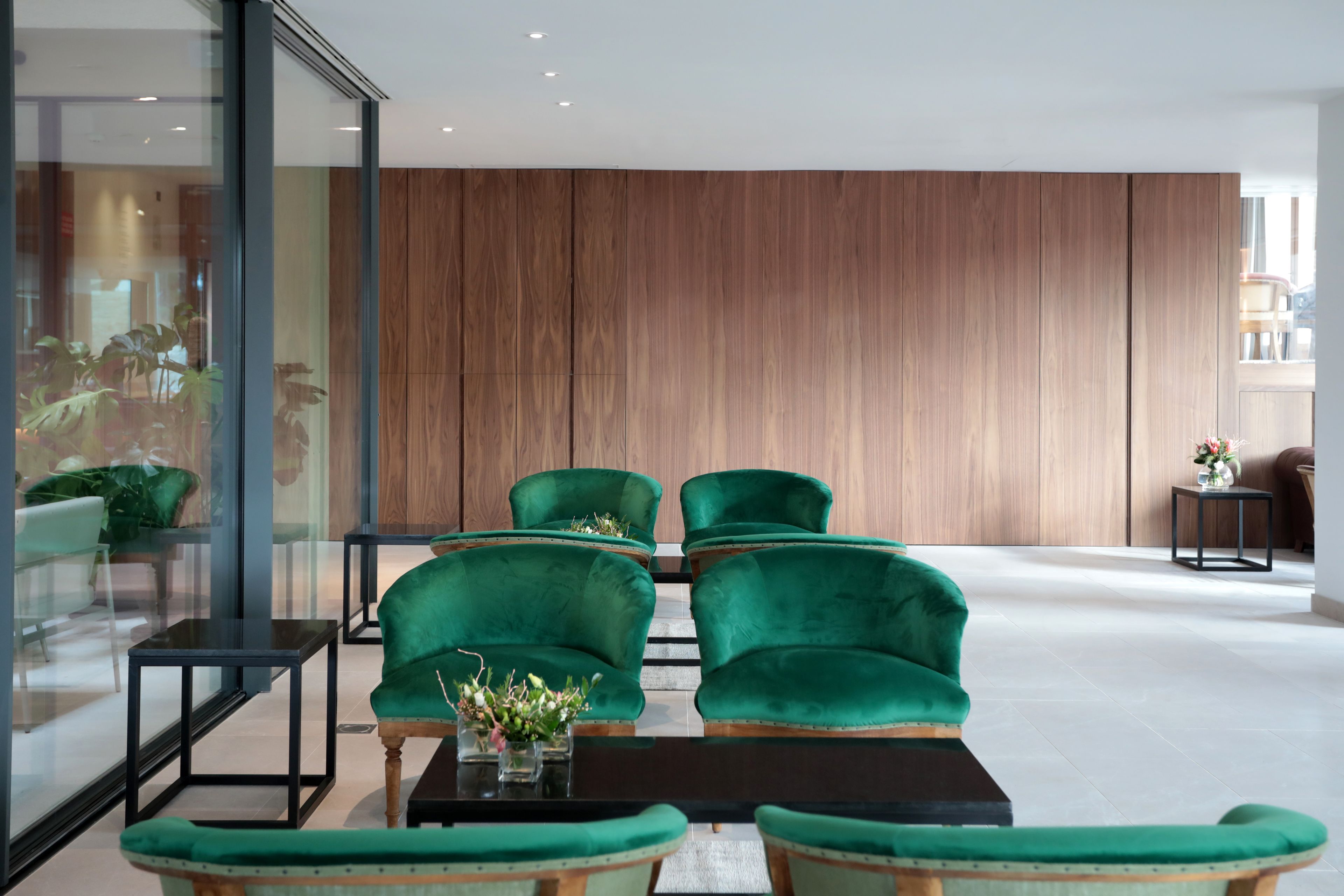 A modern lobby with green upholstered chairs, a black coffee table, and a wooden panel wall.