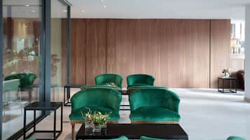 A modern lobby with green upholstered chairs, a black coffee table, and a wooden panel wall.
