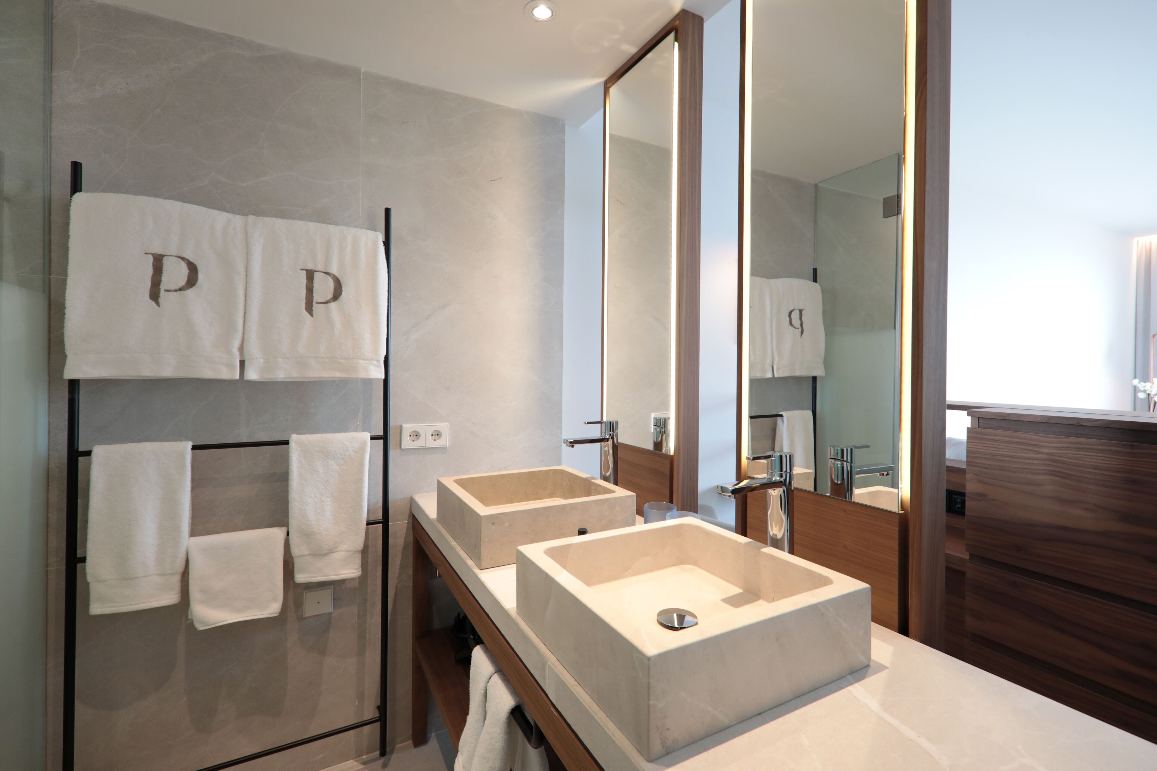 A modern bathroom with two sinks, a large mirror, and towels with 'P' monograms.