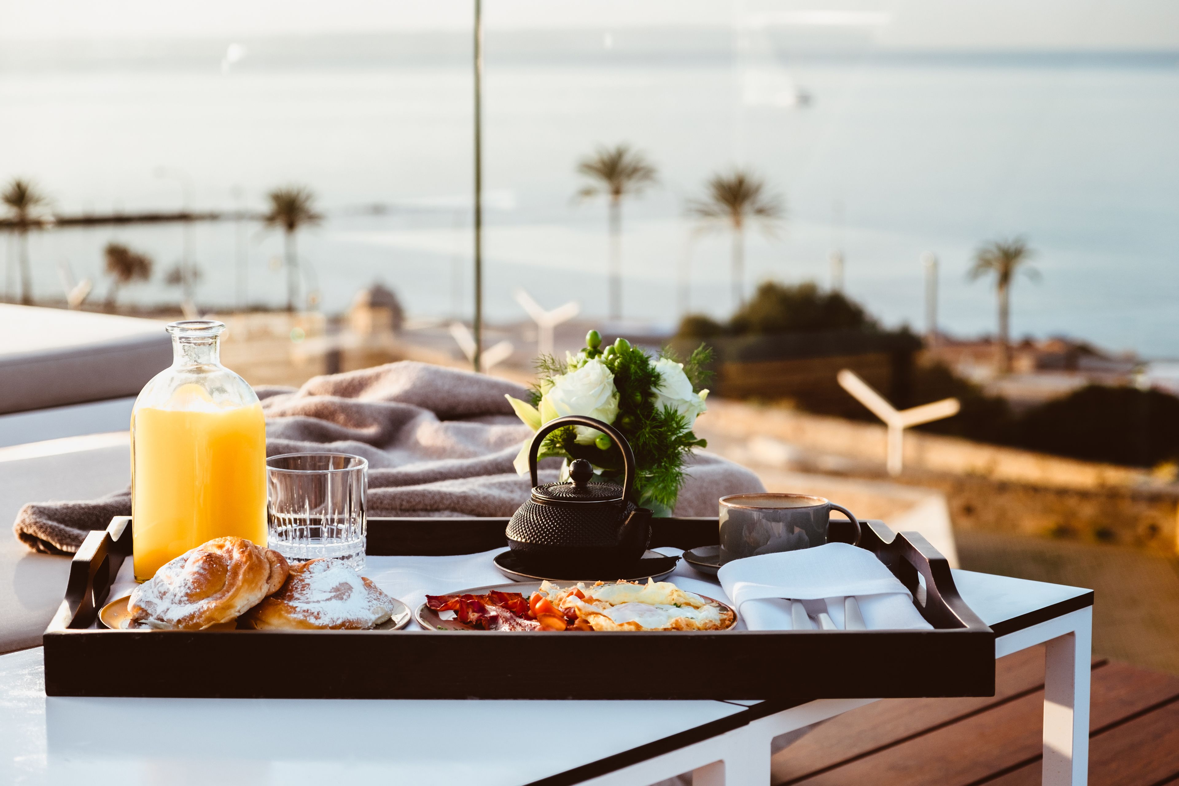 A breakfast tray with pastries, juice, and tea on a table with a view of the ocean and wind turbines in the background.