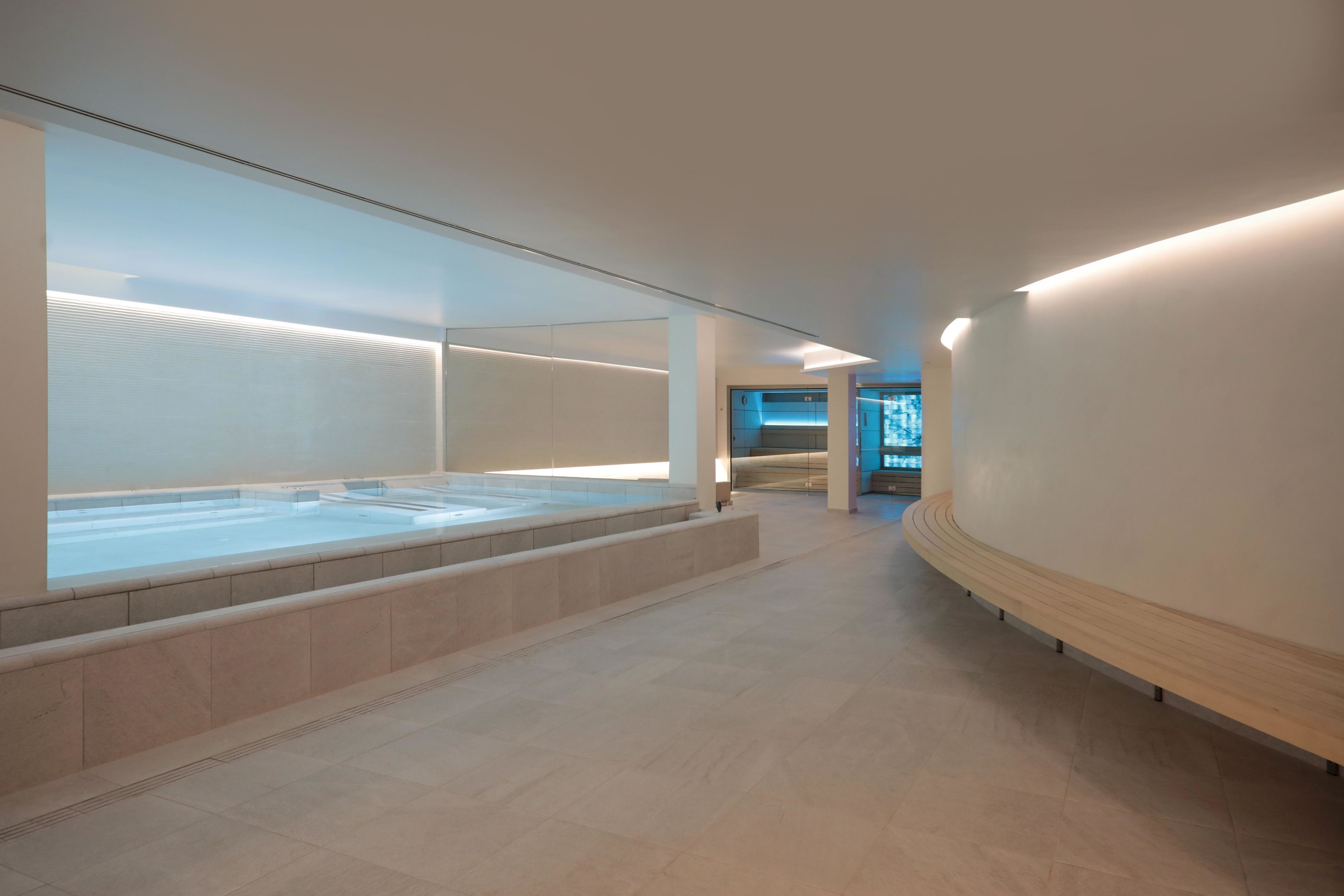 A modern spa area with a large glass-enclosed hot tub, a curved wooden bench, and a minimalist design.