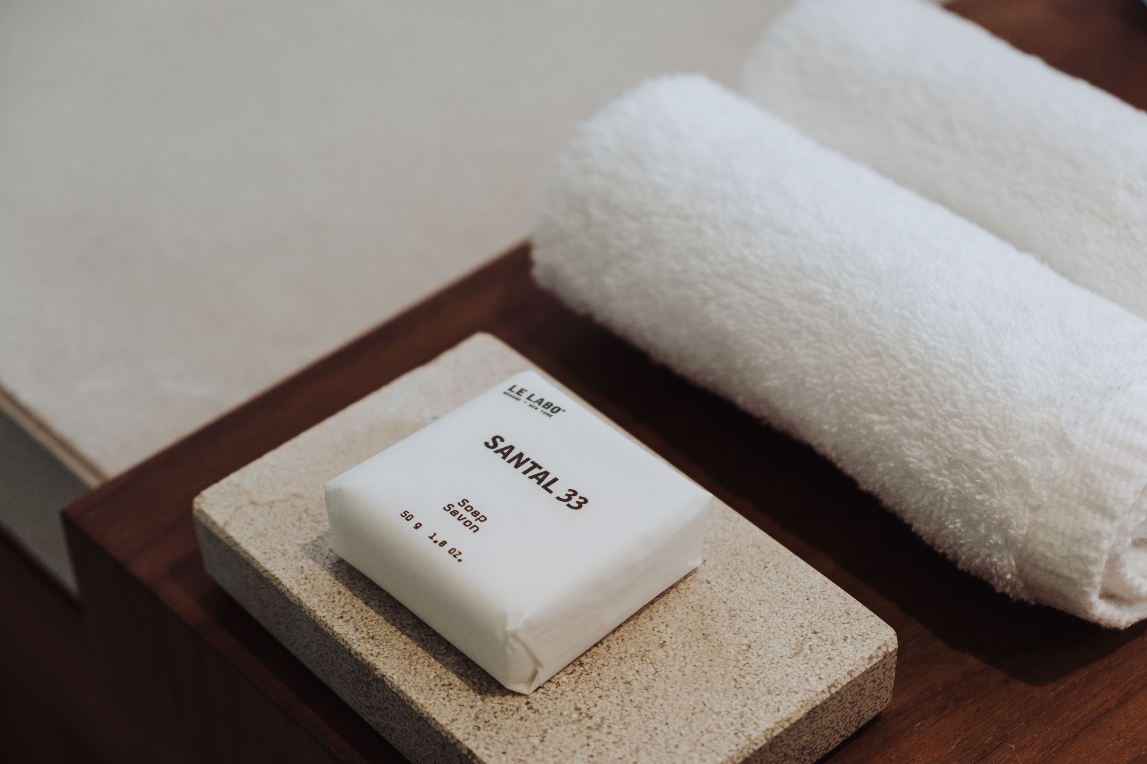Un pain de savon portant la mention « SANTAL 33 » est posé sur une surface en pierre, à côté d’une serviette blanche roulée.
