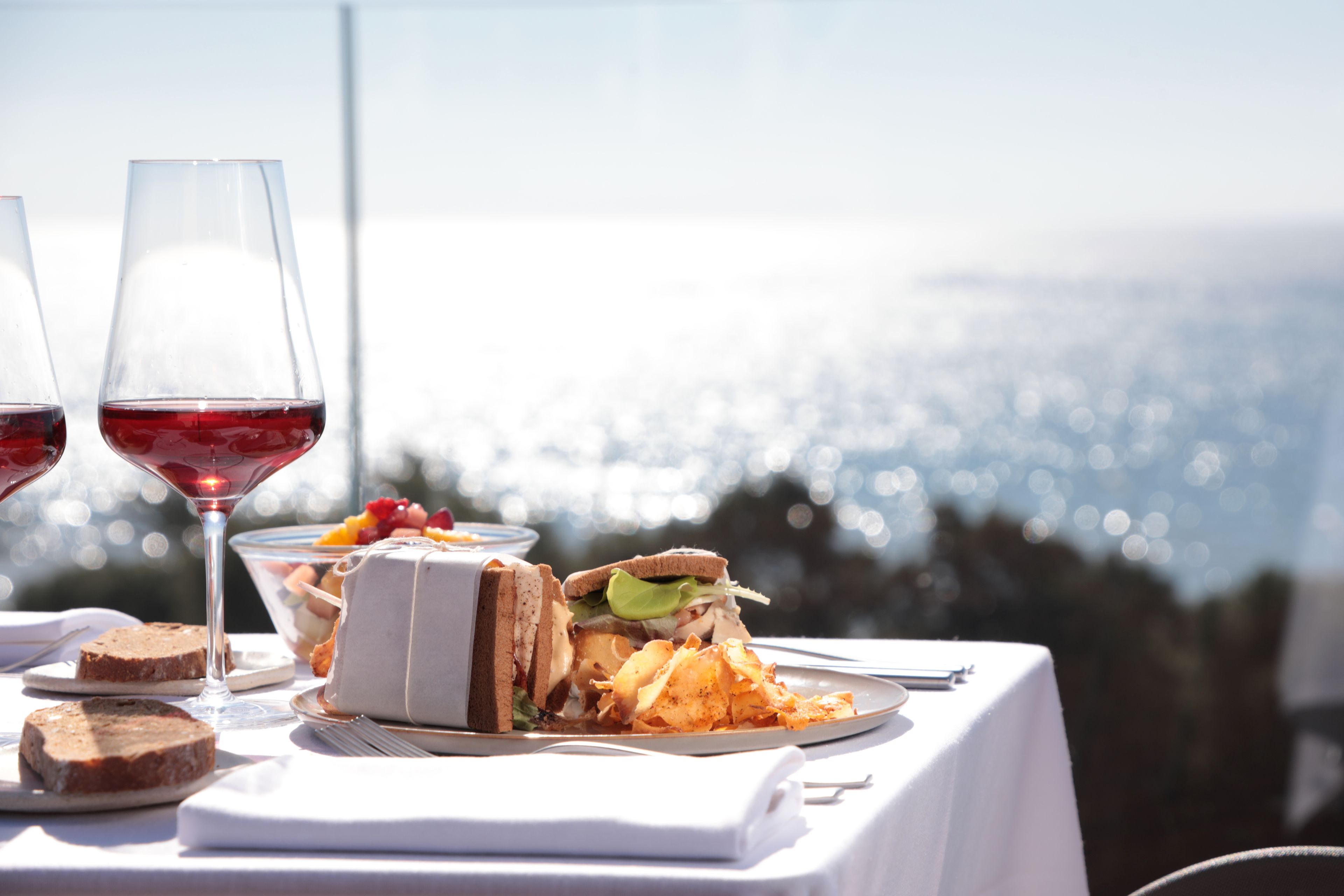 A table with food and wine glasses, a sandwich, and a dessert, set against a scenic view.