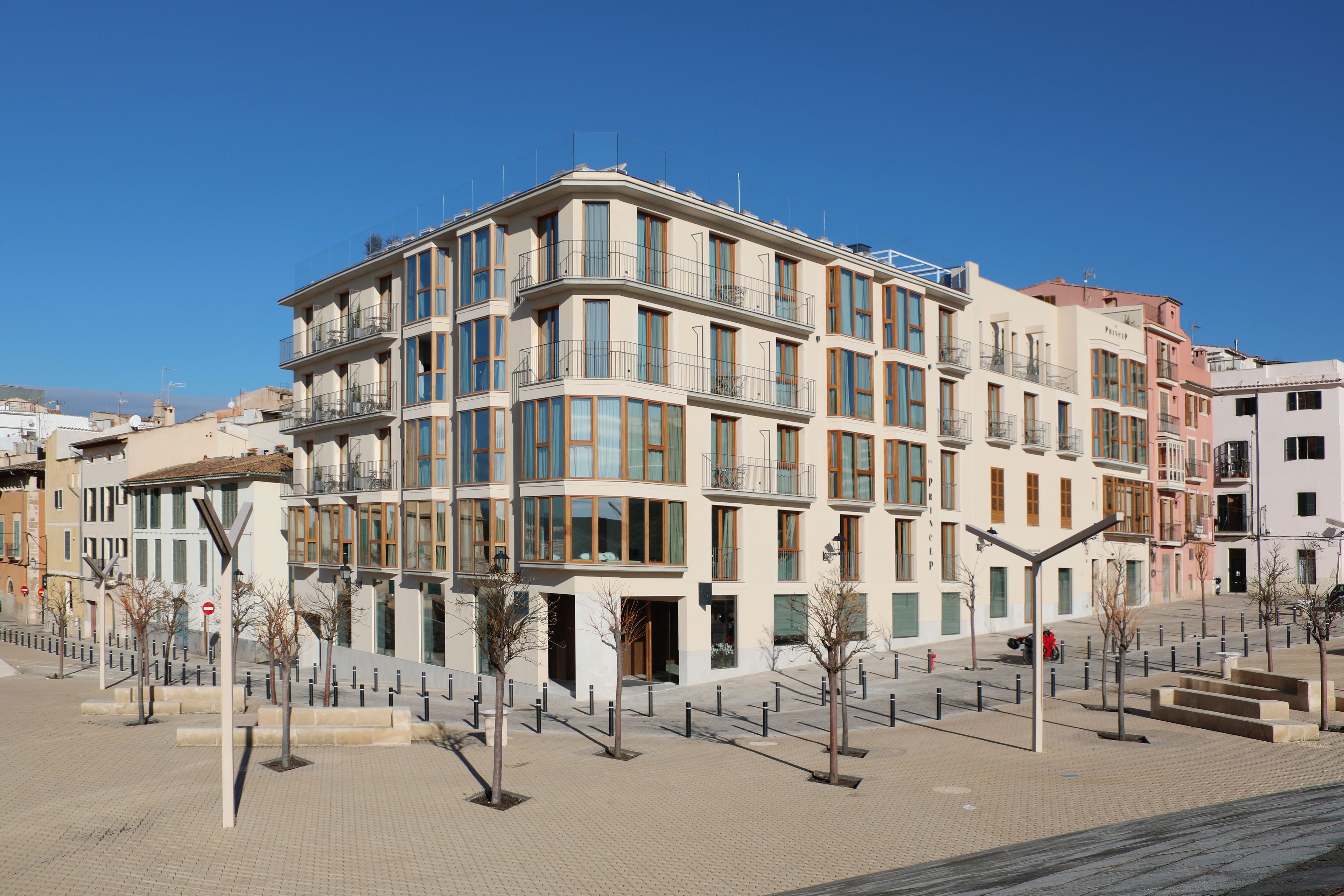 A multi-story hotel with balconies, a paved courtyard, and a clear blue sky.