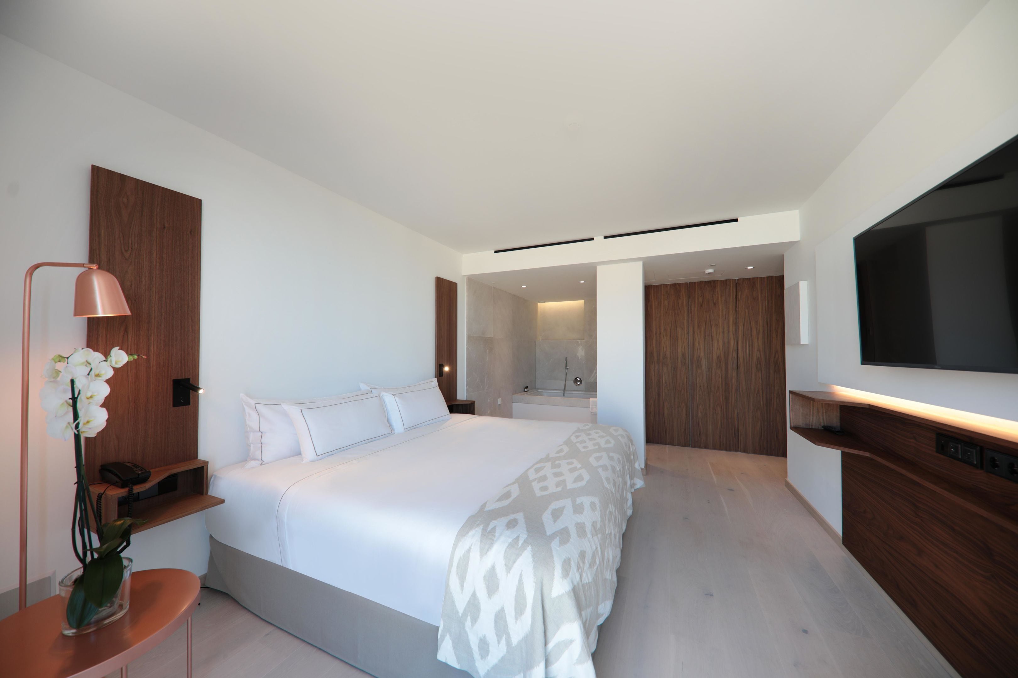 A modern hotel room with a large bed, a TV, a bathroom with a shower, and a wooden accent wall.