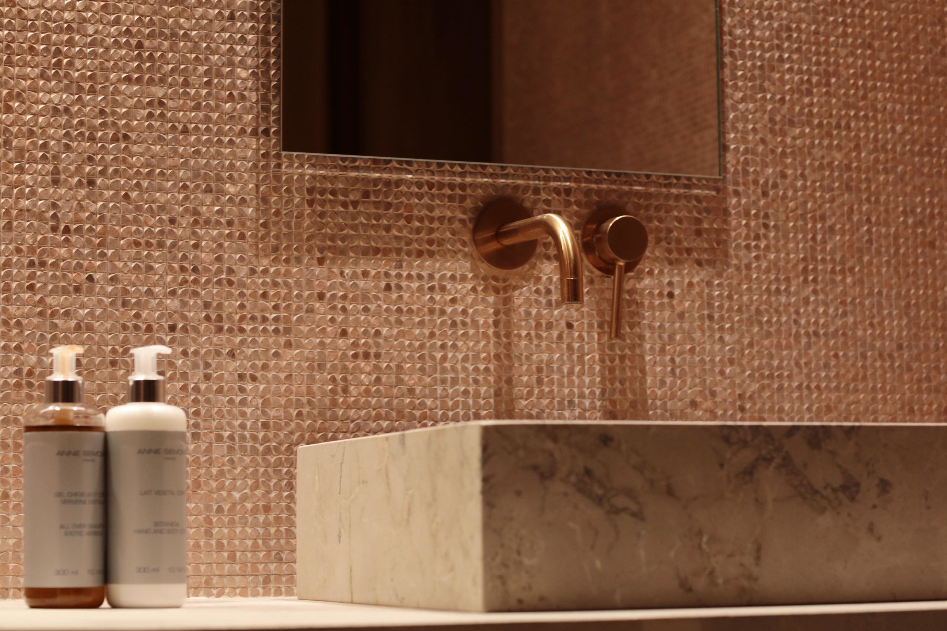 Une salle de bain avec un mur à texture, un lavabo en marbre et deux flacons de lotion.