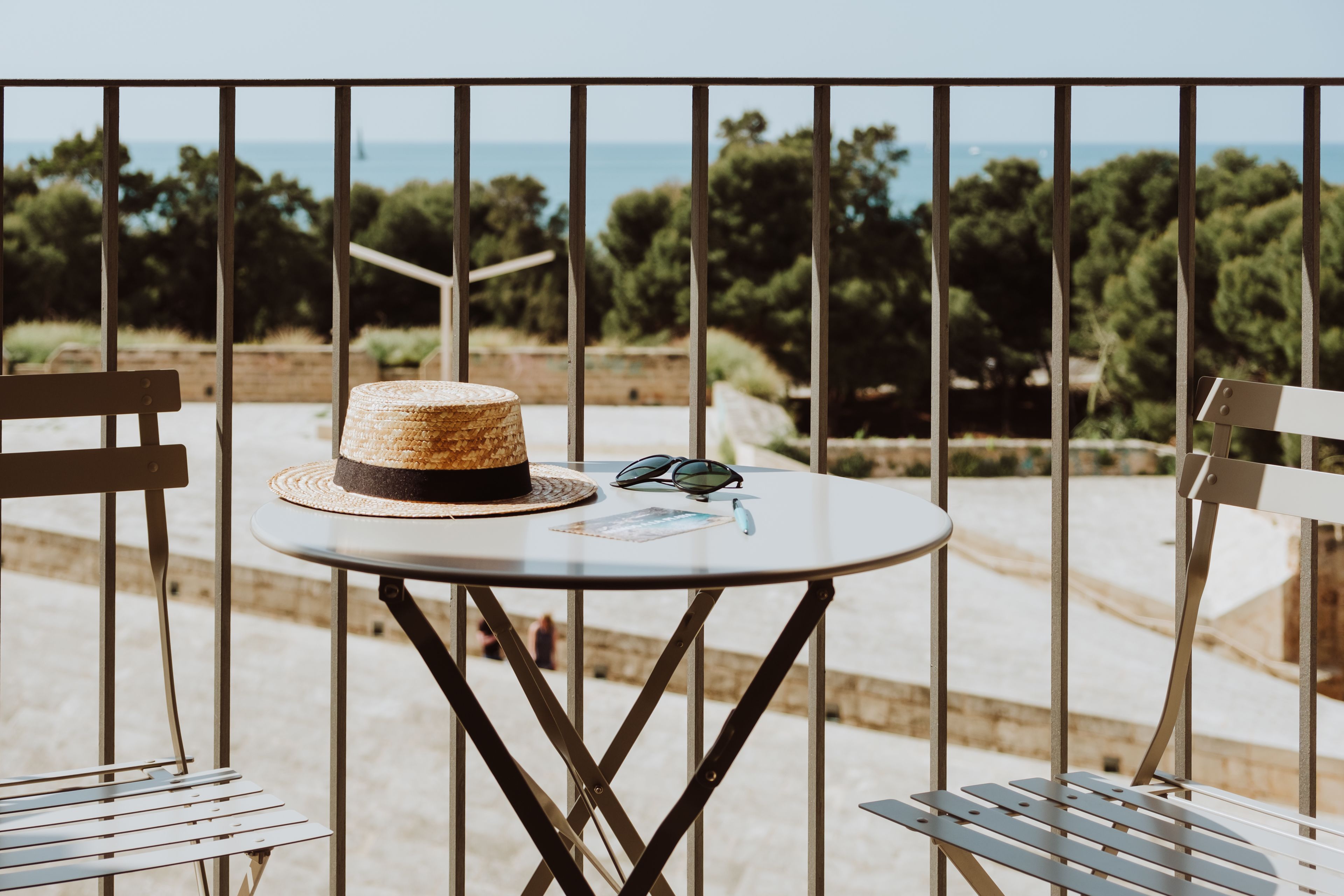 A balcony with a round table, two chairs, a straw hat, sunglasses, and a menu.
