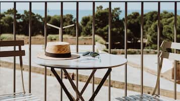 A balcony with a round table, two chairs, a straw hat, sunglasses, and a menu.