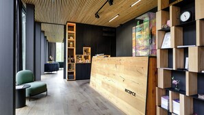Un espace d’accueil moderne avec un comptoir de réception en bois portant l’inscription « RÉCEPTION », un coin salon vert et une bibliothèque contenant divers objets.