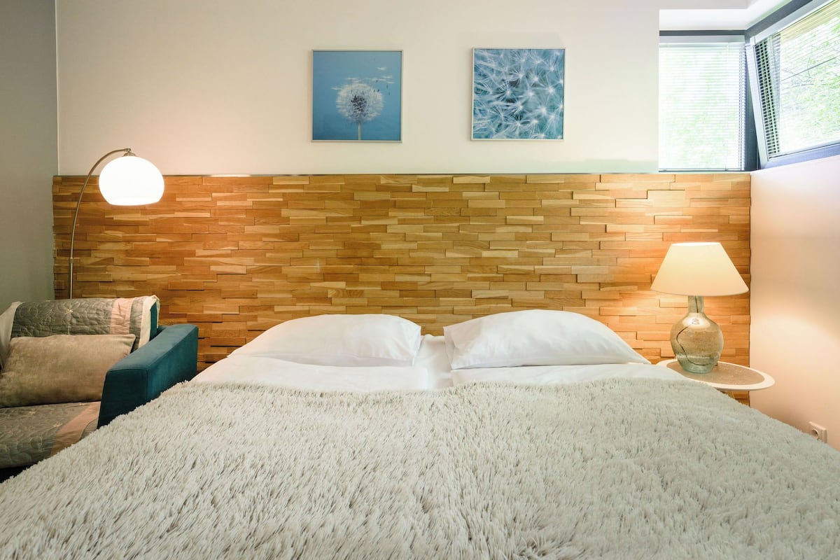 Ein Schlafzimmer mit Holz-Kopfteil, einem Bett mit weißer Bettwäsche, einem Nachttisch mit Lampe und zwei Wandbildern.