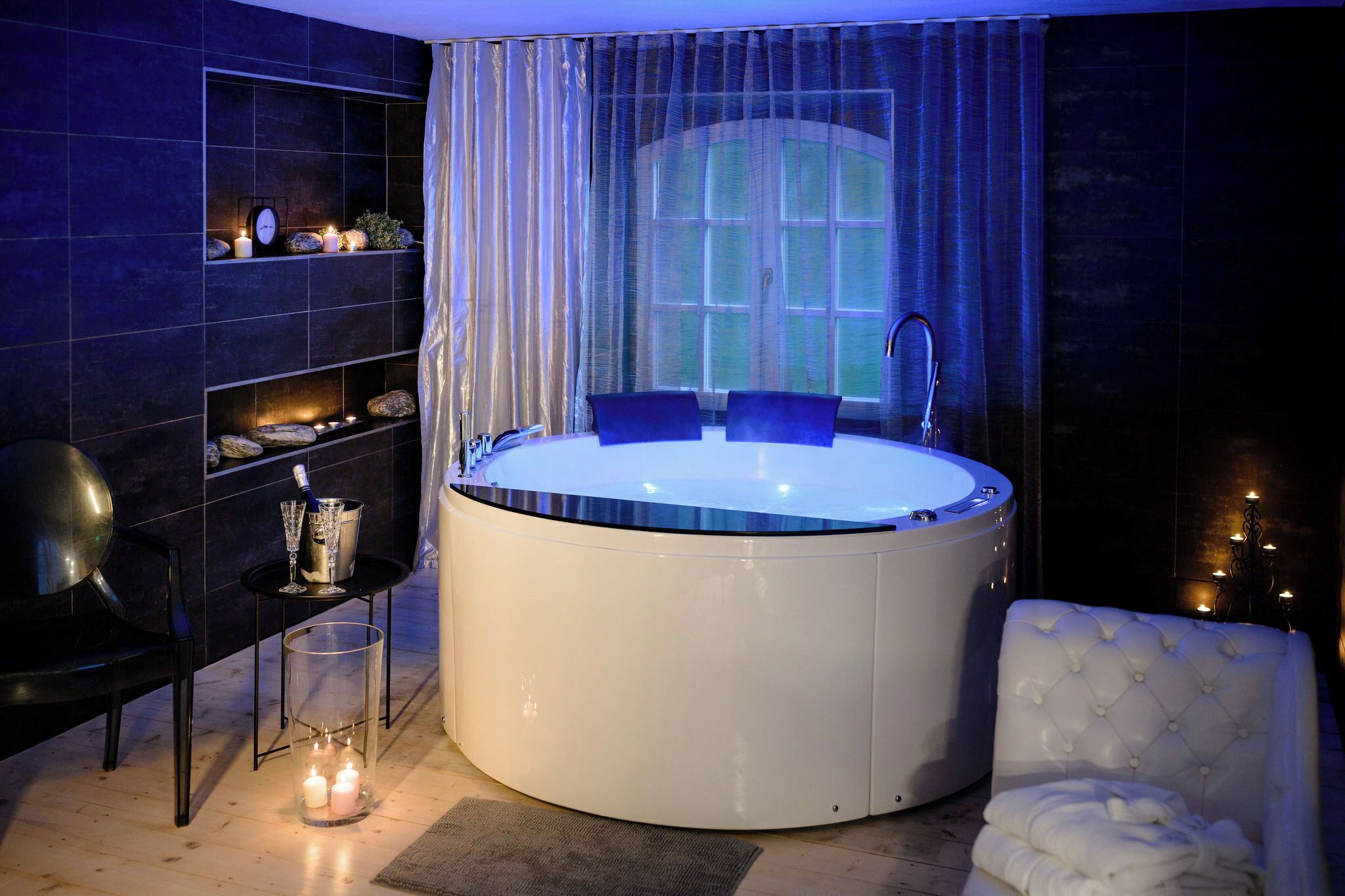 A modern bathroom with a large freestanding bathtub, a vanity with a mirror, and a seating area with a cushioned chair.