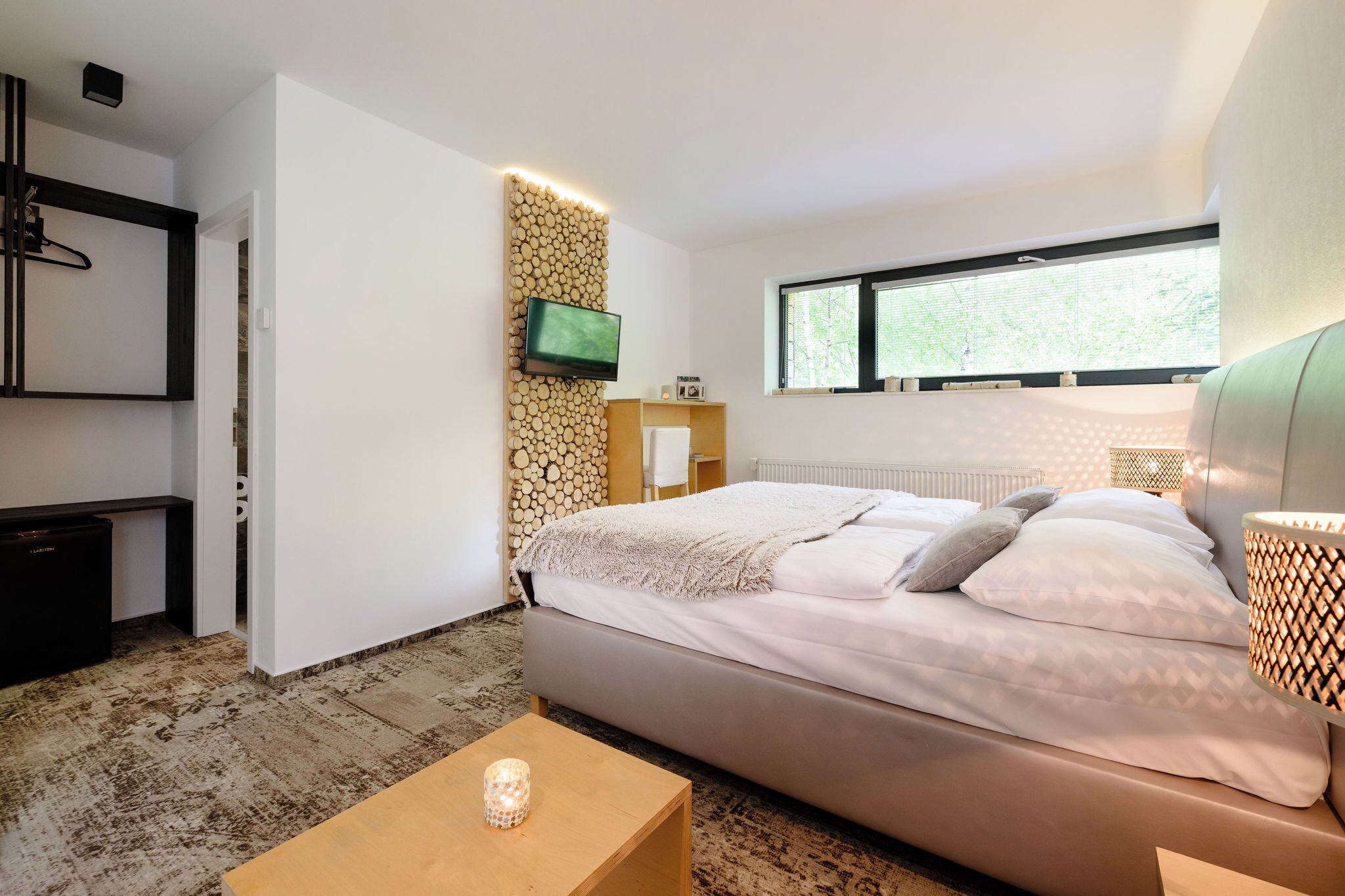 A modern bedroom with a bed, bedside table, TV, and a window with a view.