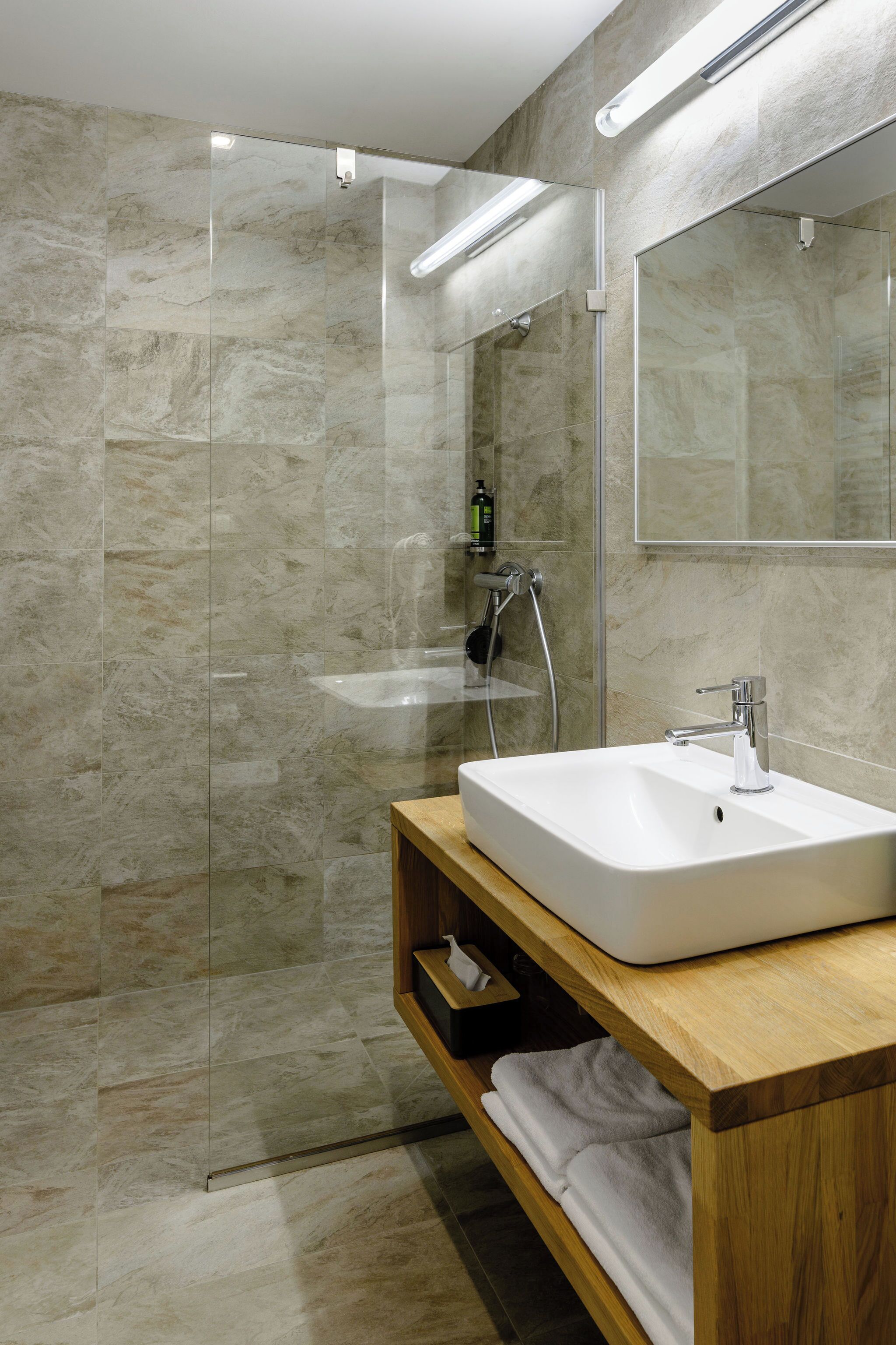 A modern bathroom with a glass shower enclosure, a white sink, and a wooden vanity.
