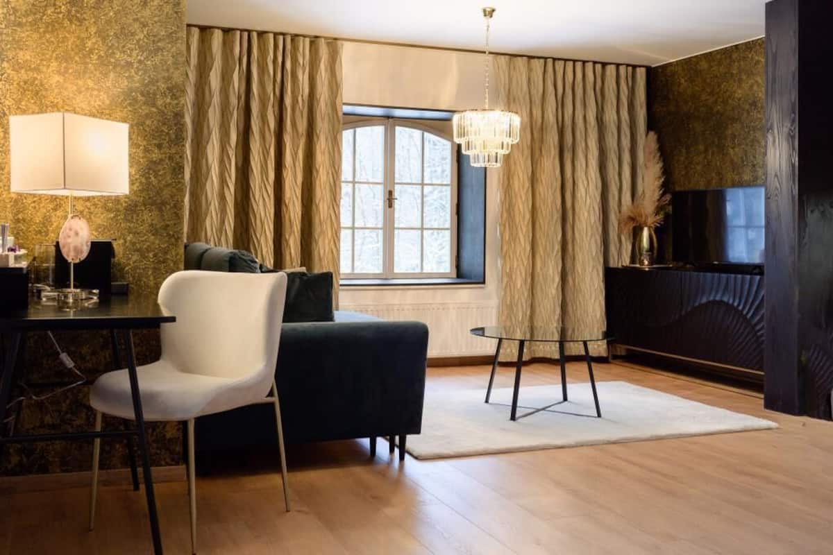 Ein modernes Wohnzimmer mit einem dunklen Sofa, einem weißen Sessel, einem kleinen Tisch und einem großen Fenster mit Vorhängen.