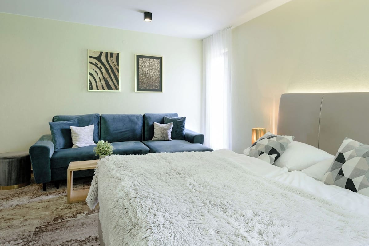 Ein modernes Schlafzimmer mit einem blauen Sofa, einem weißen Bett und zwei Wandbildern.