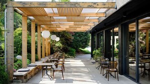 Une terrasse extérieure dotée d’une pergola en bois, de tables et de chaises, le tout entouré de verdure.