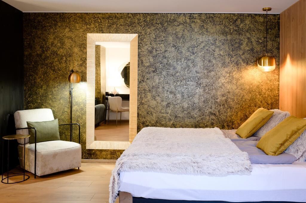 A bedroom with a large bed, a chair, a desk, and a mirror.