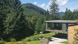 Un bâtiment moderne à la façade de verre, entouré d’une végétation luxuriante et surplombé d’un ciel bleu azur.