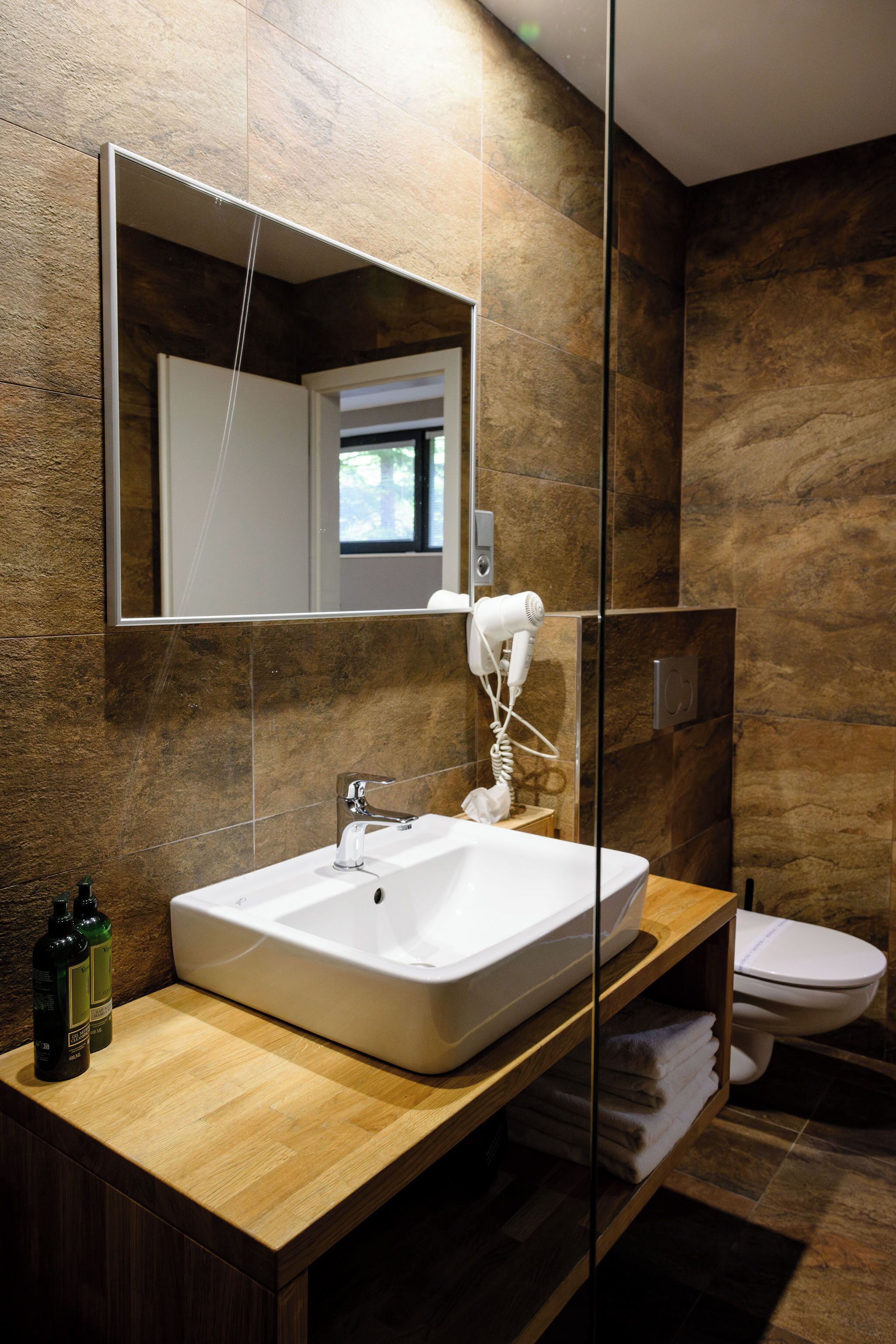 A modern bathroom with a large mirror, a white sink, and a hairdryer mounted on the wall.