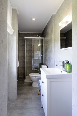 Een moderne badkamer met een douchecabine van glas, een wit toilet en een wastafel met spiegel en groene flessen.
