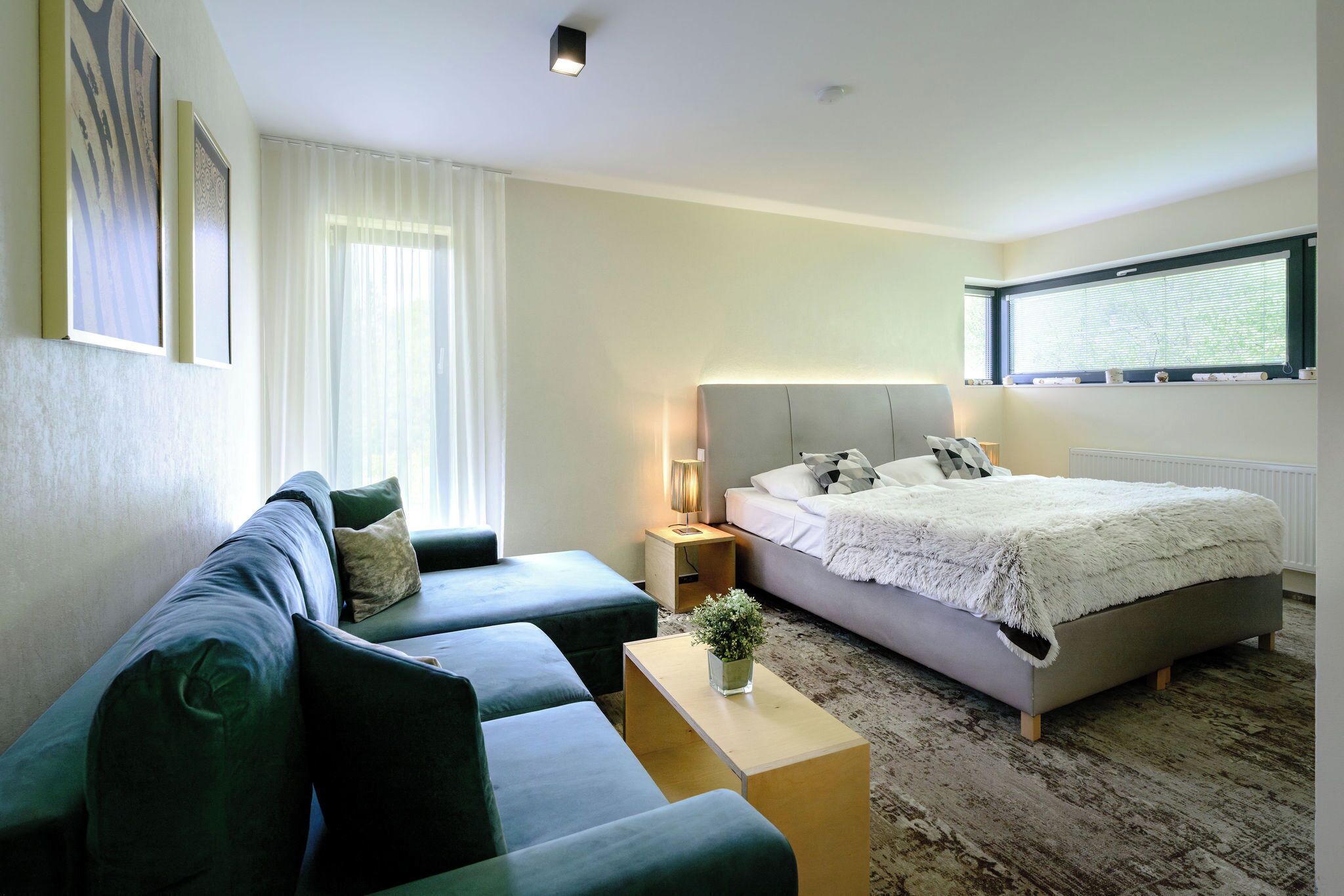 Una habitación de hotel moderna con cama, sofá, mesita de noche y ventana con persianas.