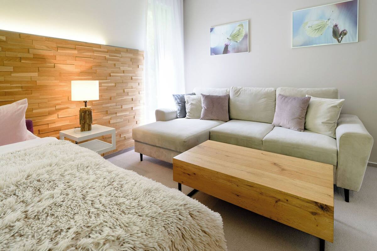 Ein modernes Hotelzimmer mit einer Wand aus Holzpaneelen, einer Sofagarnitur, einem flauschigen Teppich und einem Holztisch.