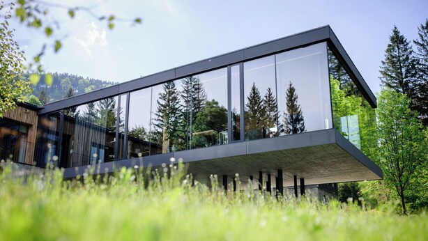 Un bâtiment moderne doté de grandes fenêtres en verre, d’un toit plat et d’une base en béton.