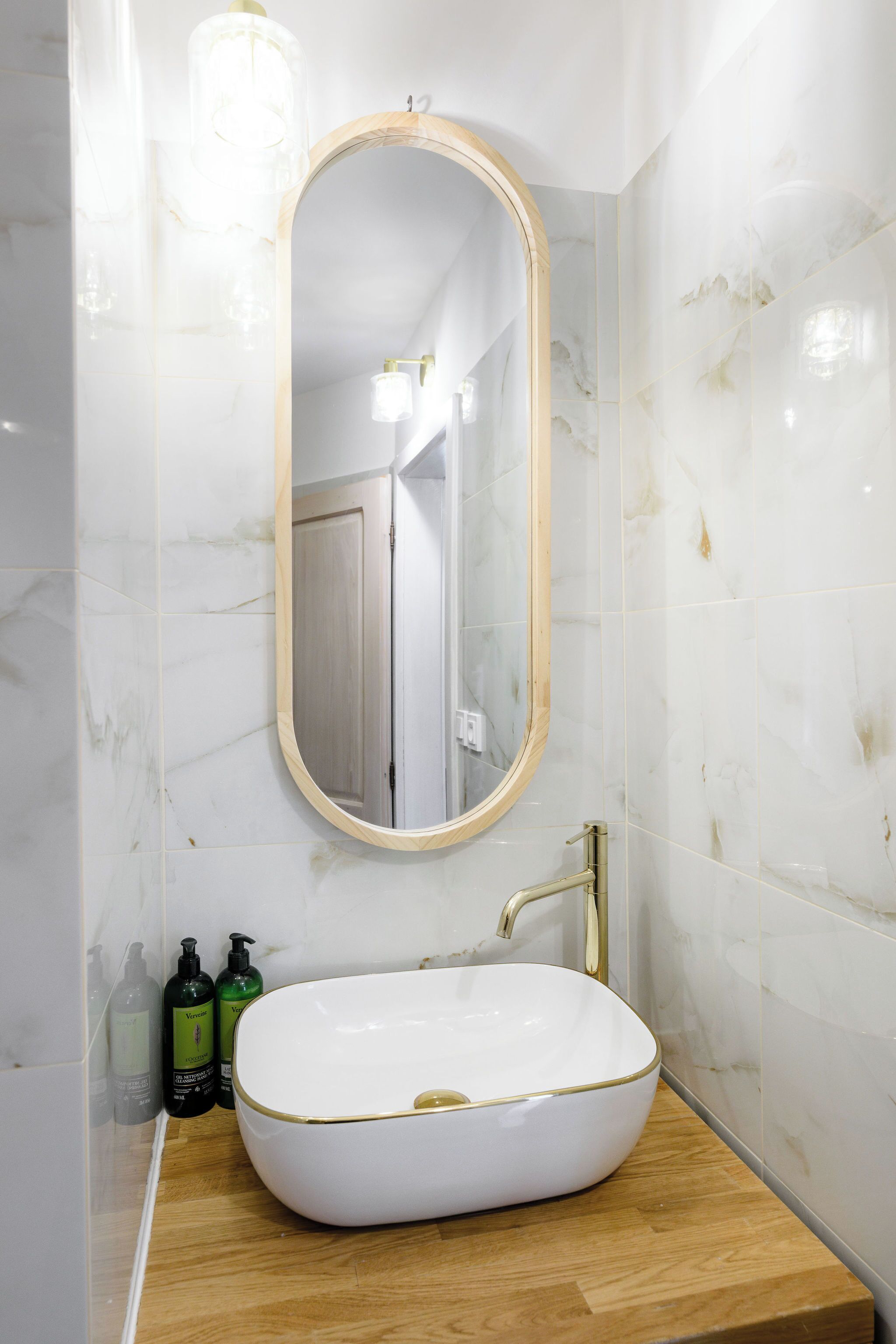 A bathroom with a white oval sink, a wooden-framed mirror, and marble walls.
