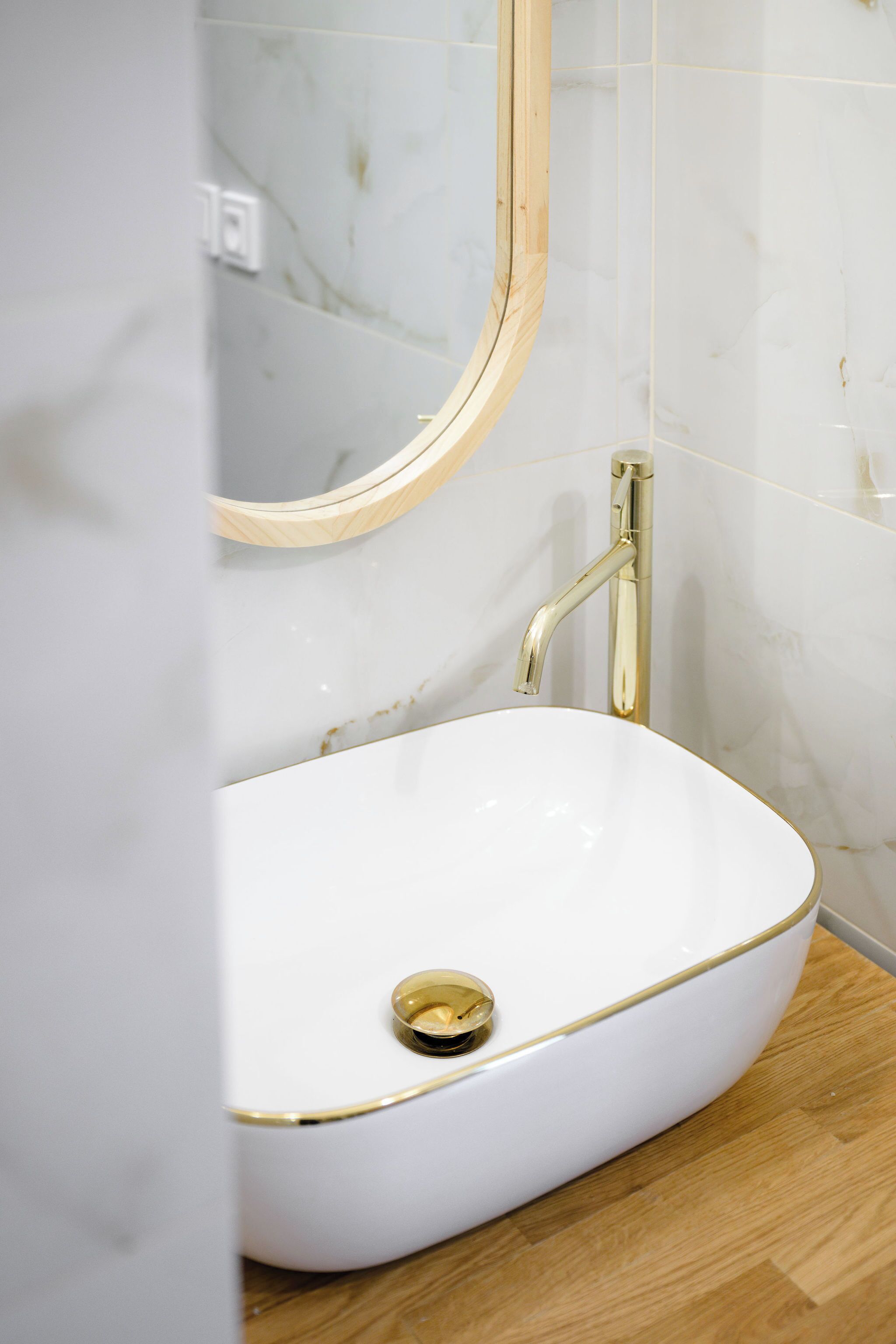 A bathroom with a white oval sink, gold trim, and a wooden vanity.
