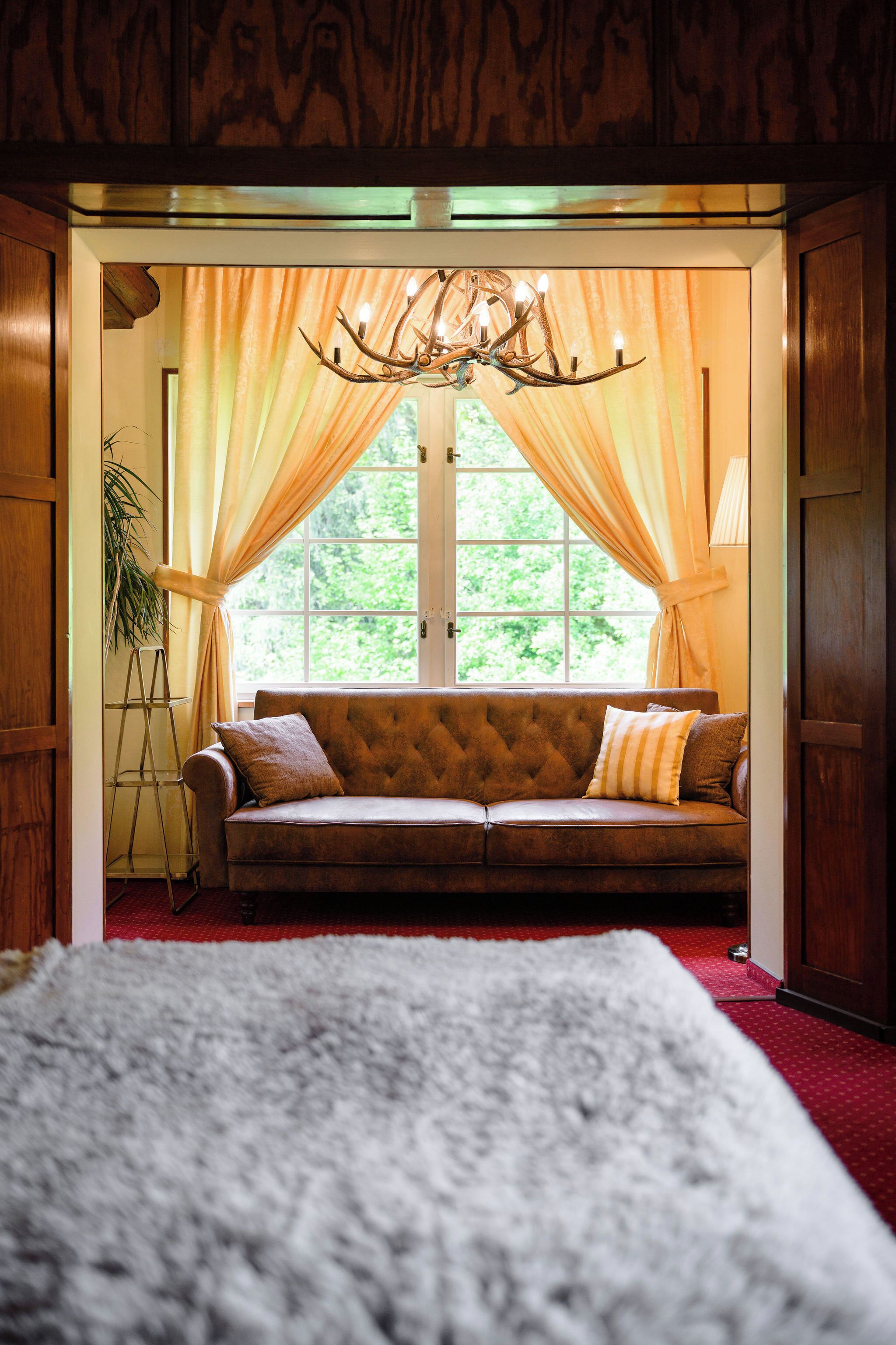 A cozy room with a large window, a wooden ceiling, and a plush sofa with cushions.