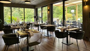 Un espace de restauration moderne avec des tables et des chaises en bois, de grandes fenêtres donnant sur un paysage verdoyant et un éclairage suspendu.