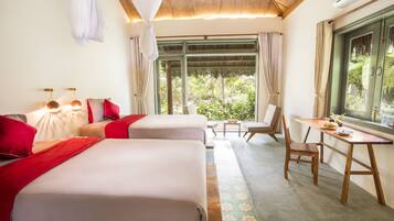 A hotel room with two beds, a dining table, and a view of greenery outside.