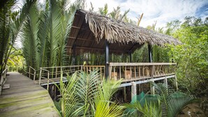 A wooden structure with a thatched roof surrounded by lush greenery. - Mekong Home (Phuoc Long)